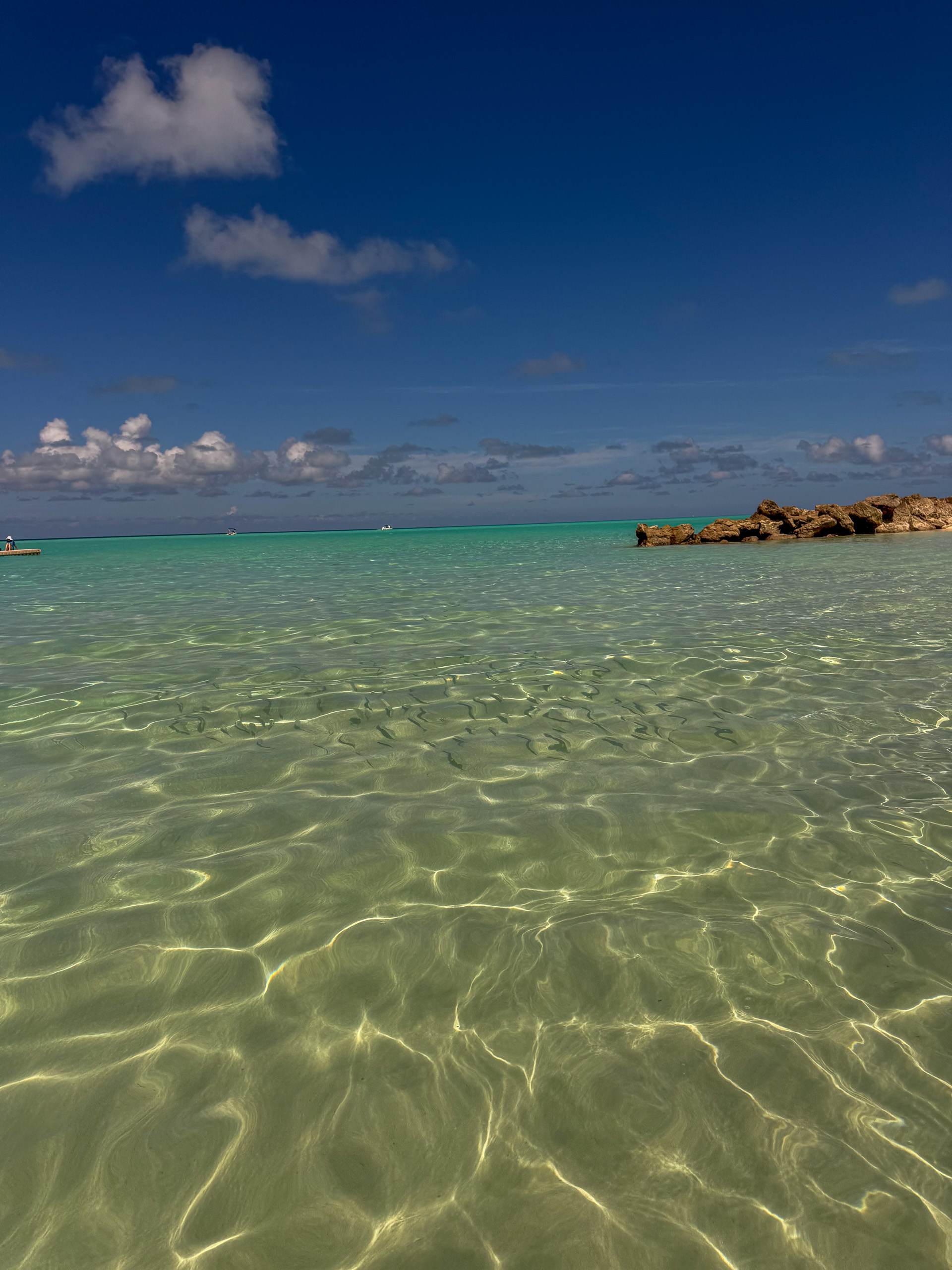 Clear water over rippled sand, rock breaking through at the edge