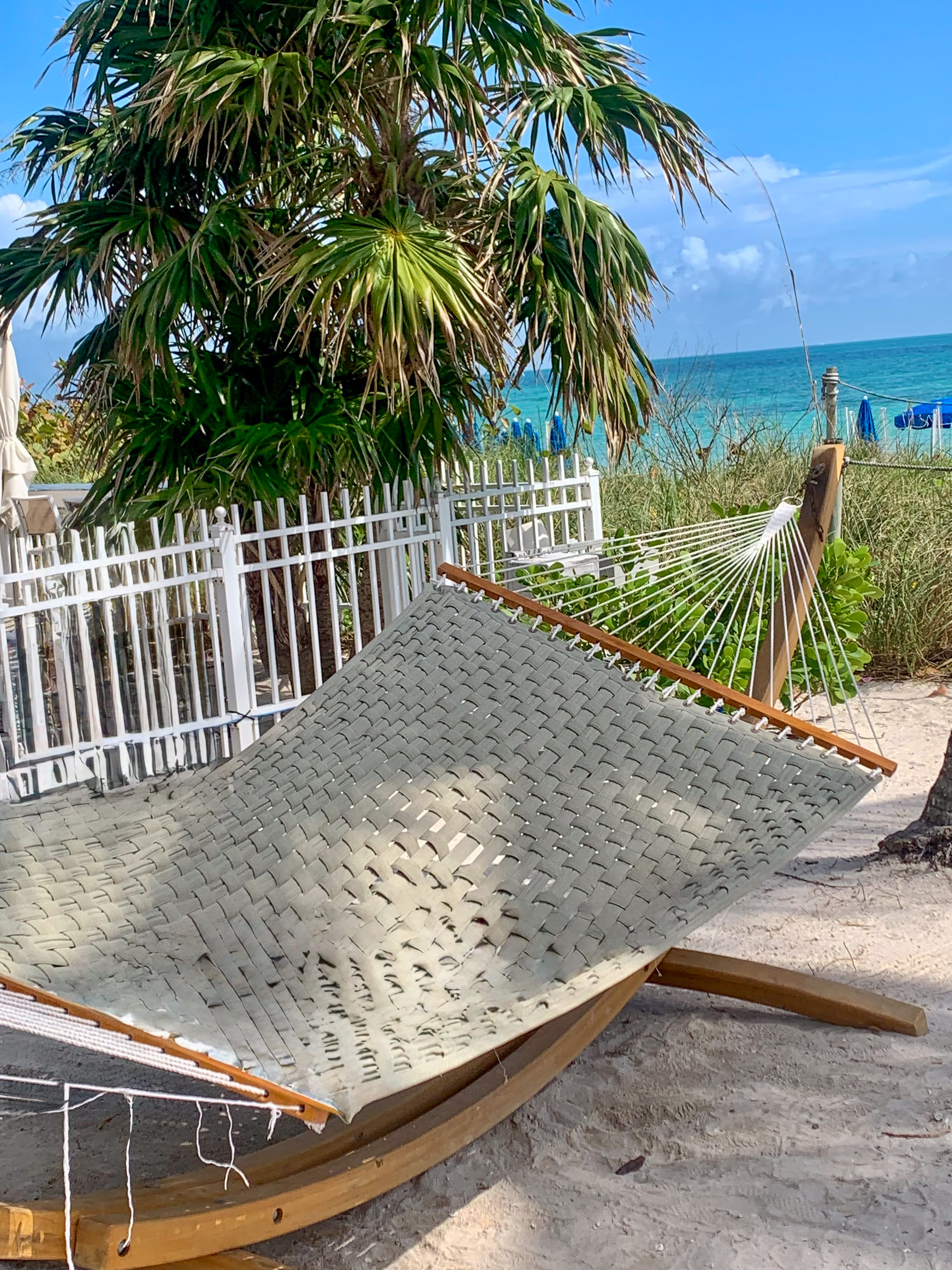 A rope hammock strung on the boardwalk above the sand, the sea beyond the rail
