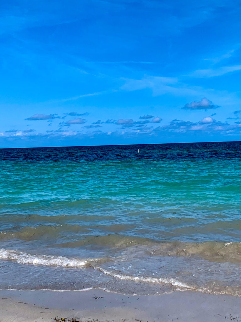 Turquoise water breaking on the sand, the shelf of deeper blue behind it
