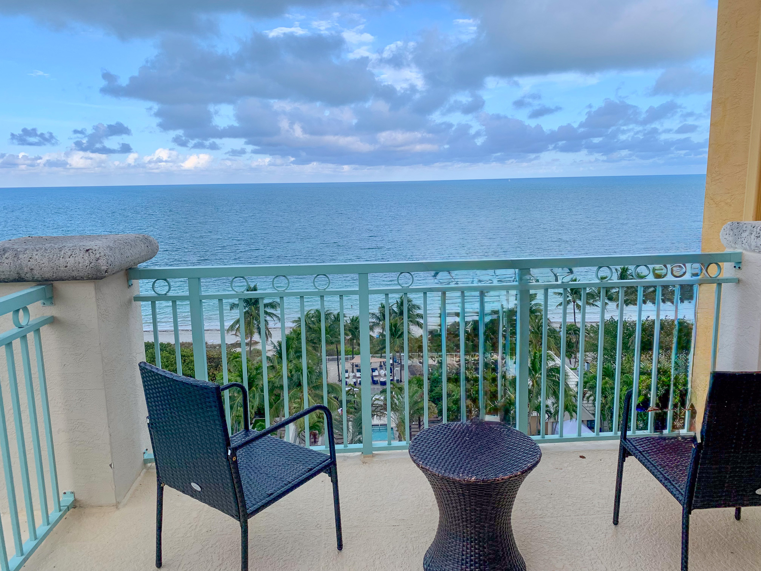 Two chairs and a small table on the balcony, the sea filling the gap in the rail