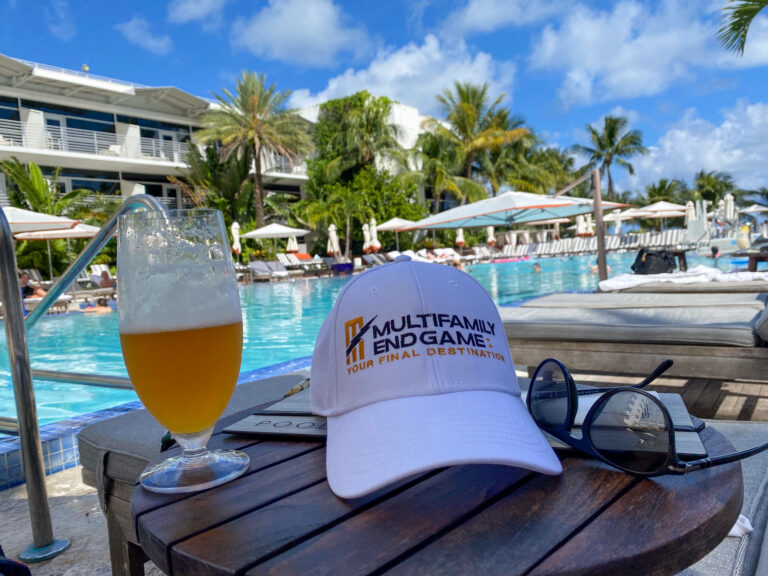 A glass of beer and a cap on a table by the pool, loungers and palms beyond