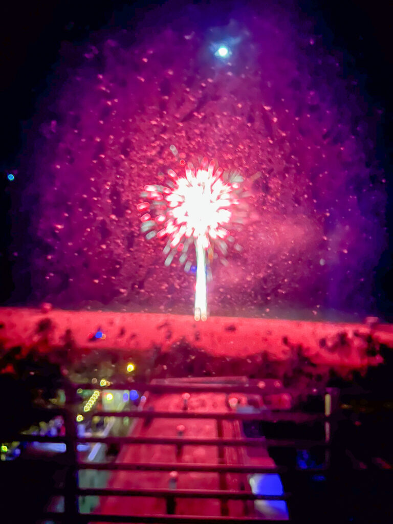 A firework bursting pink and white over the beach, the boardwalk lit below