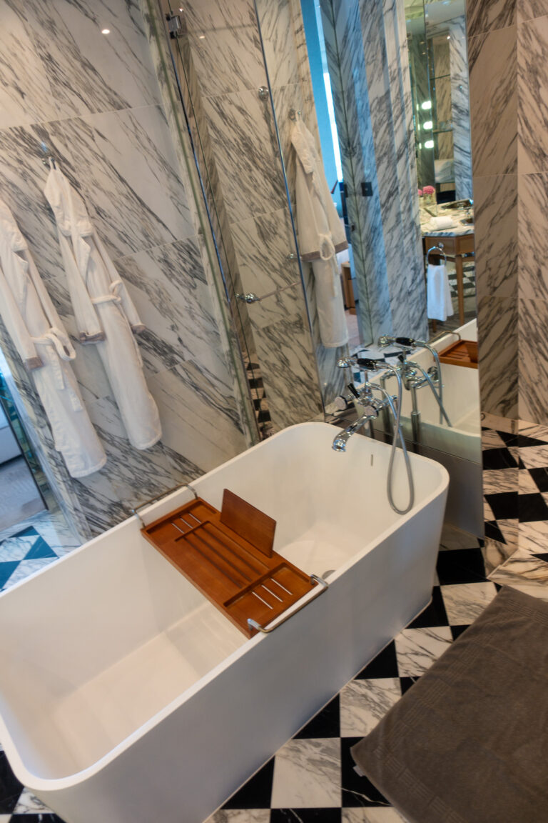 A freestanding tub with a timber tray, robes hanging on the marble wall