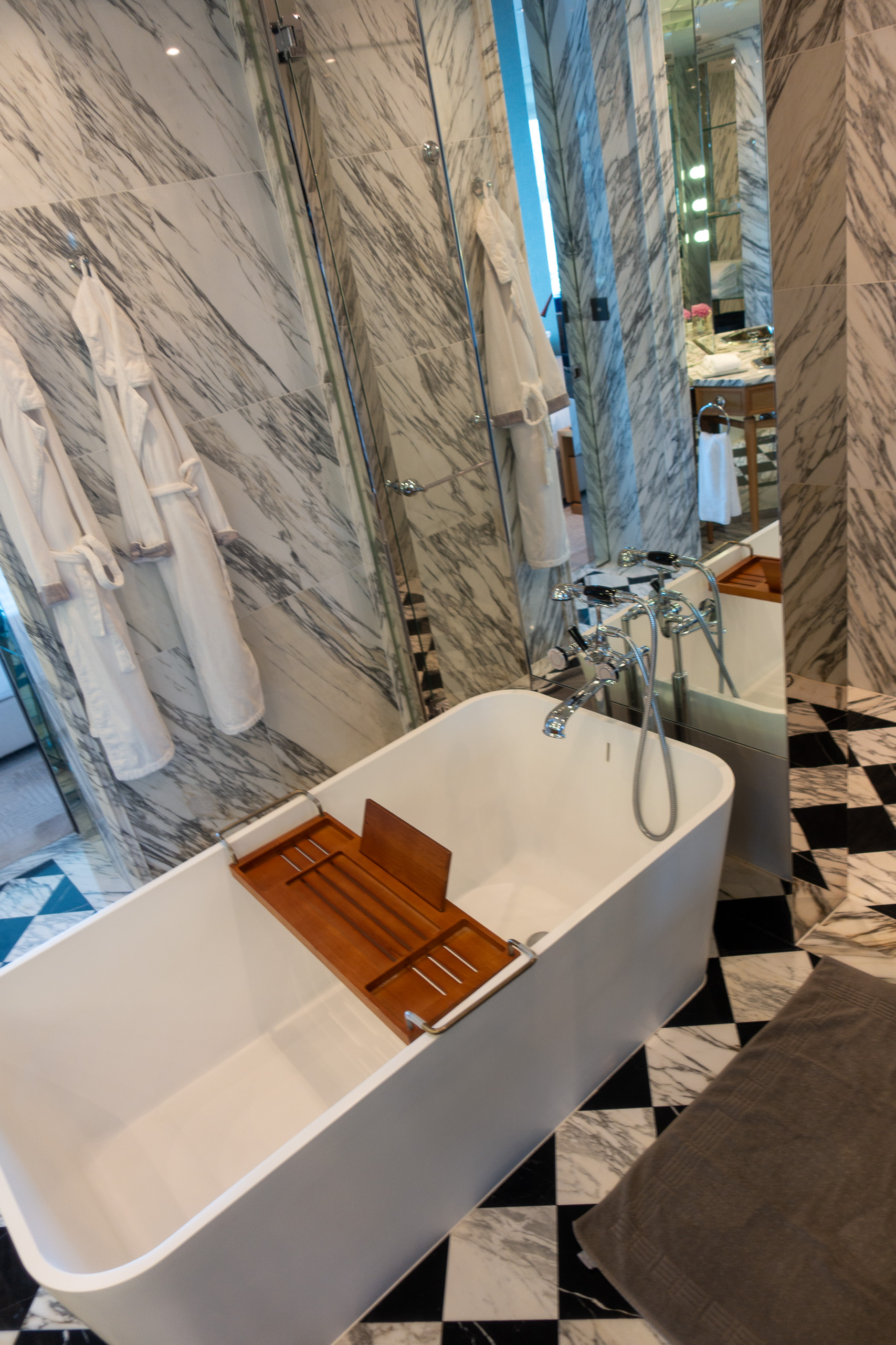 A freestanding tub with a timber tray, robes hanging on the marble wall