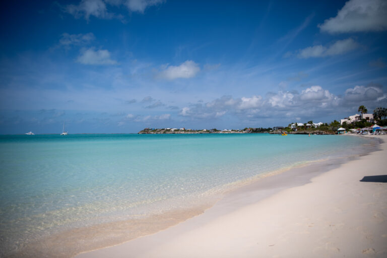 Flat calm water off the beach, a sailboat anchored in the distance