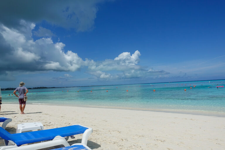 A figure walking the waterline, loungers behind on the sand