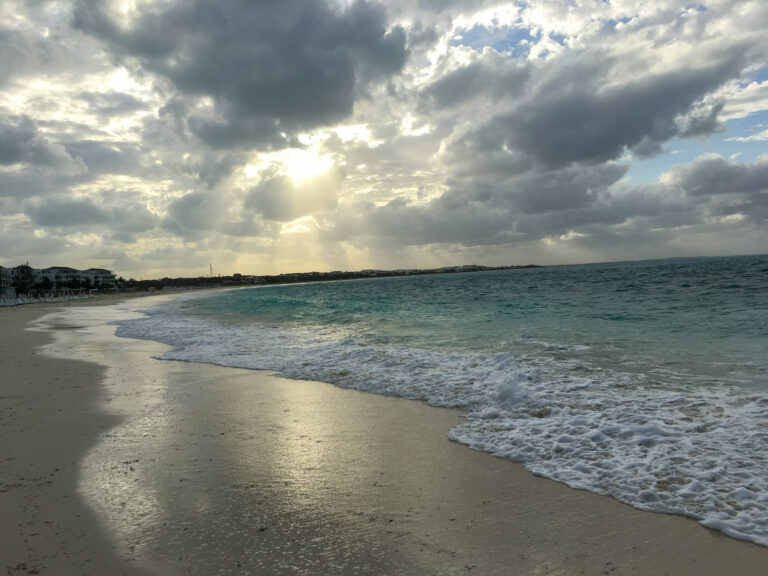 The sun breaking through cloud over the wet sand at dusk