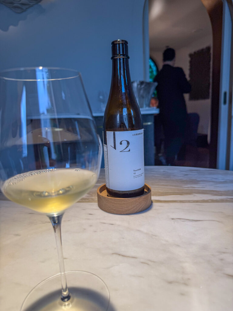 A glass of white wine poured at the table, the bottle behind