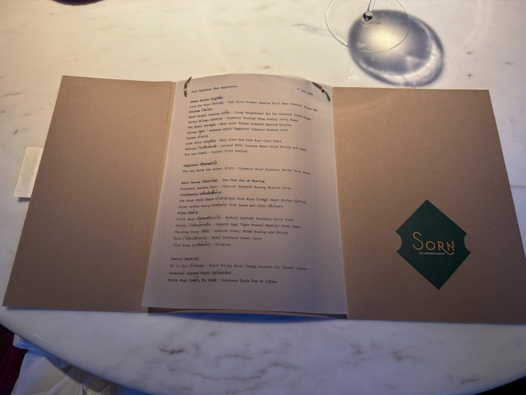 The tasting menu open inside its grey folder, courses listed in Thai and English beside the green Sorn diamond