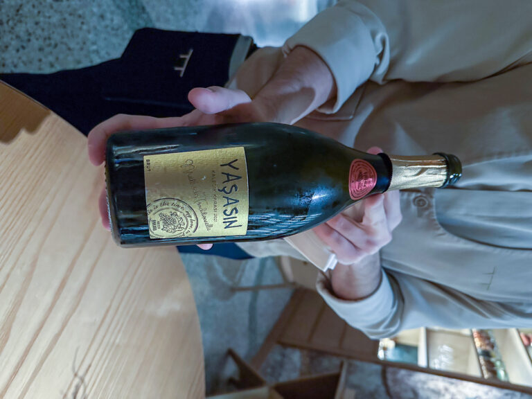 A bottle of Yasasin sparkling wine held out across the table
