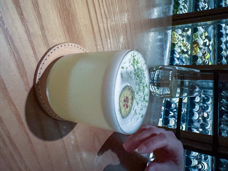 A pale green cocktail dressed with herbs, held above the counter