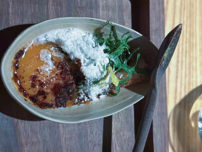 A dish under orange sauce and white crumb with herbs, in a pale bowl