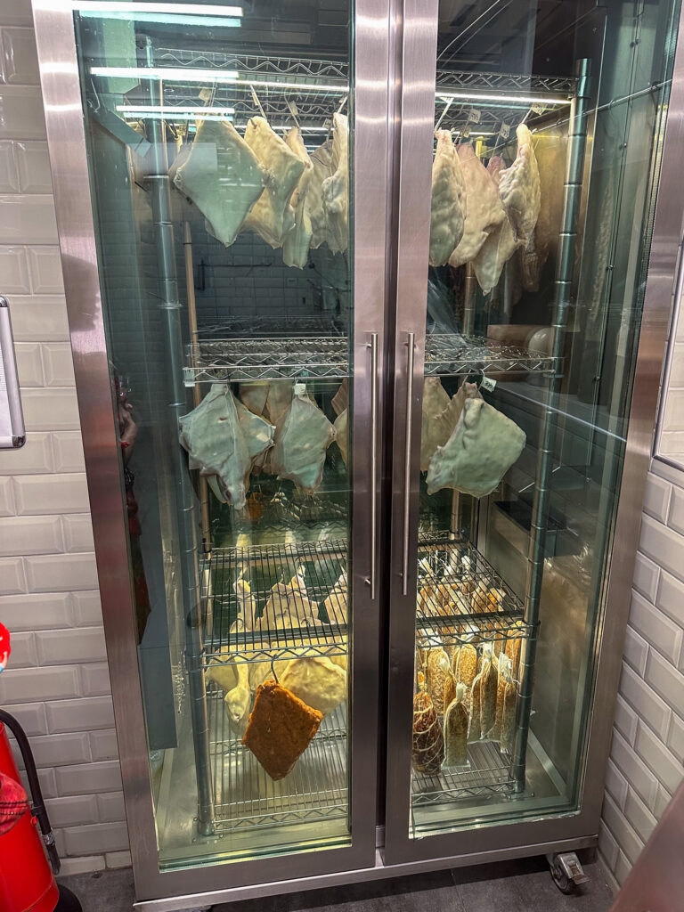 Two glass-fronted cabinets hung with drying fish and flatbreads on wire racks