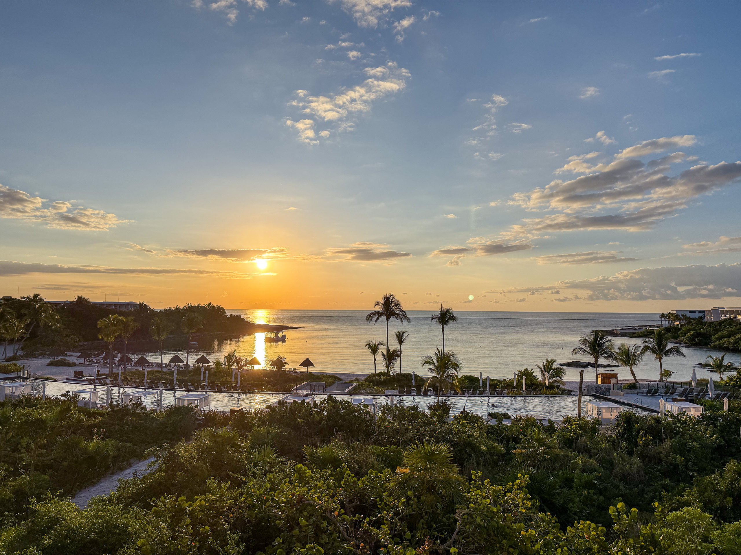 The sun going down over the sea beyond the palms and the roofs of the resort