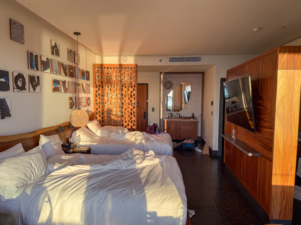 A room with two beds made up in white, orange curtains and a timber wall