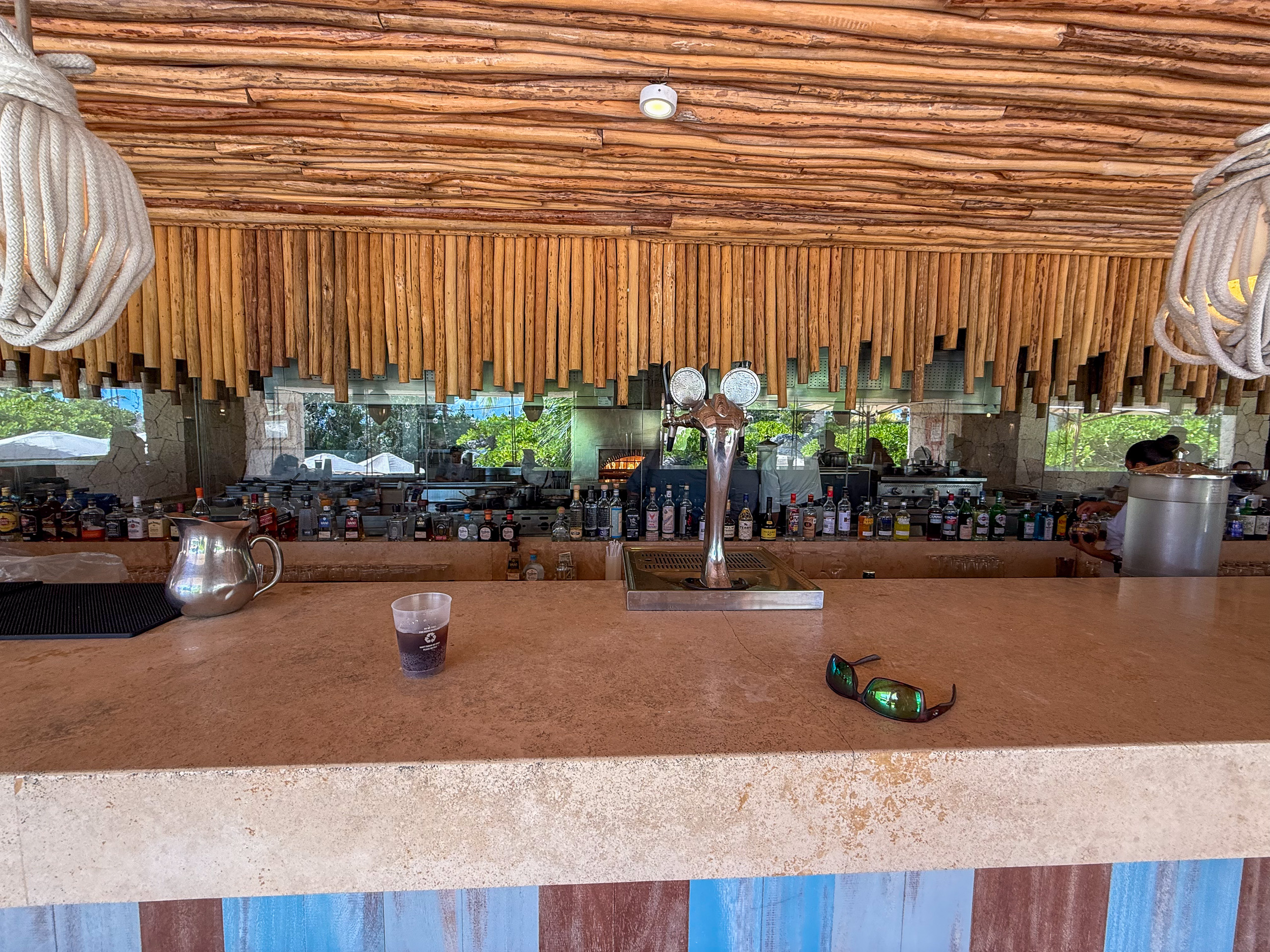 A long bar counter under a reed ceiling, bottles ranged along the back