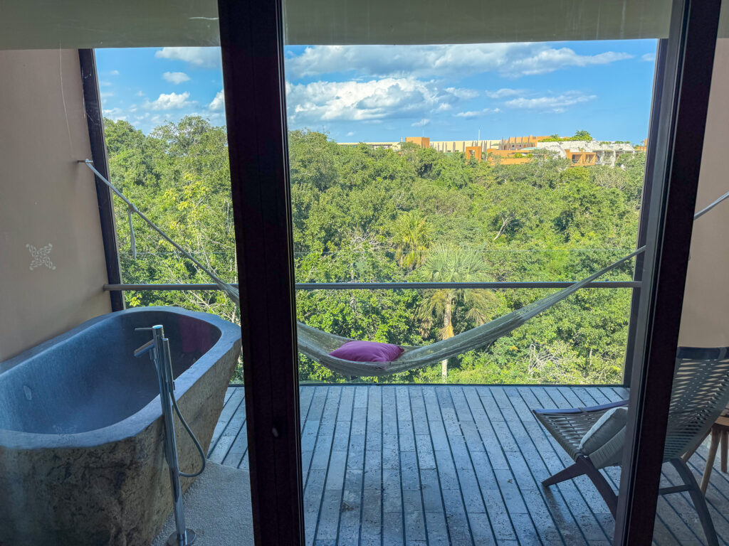 A freestanding bath at the window, a hammock strung on the deck and jungle beyond