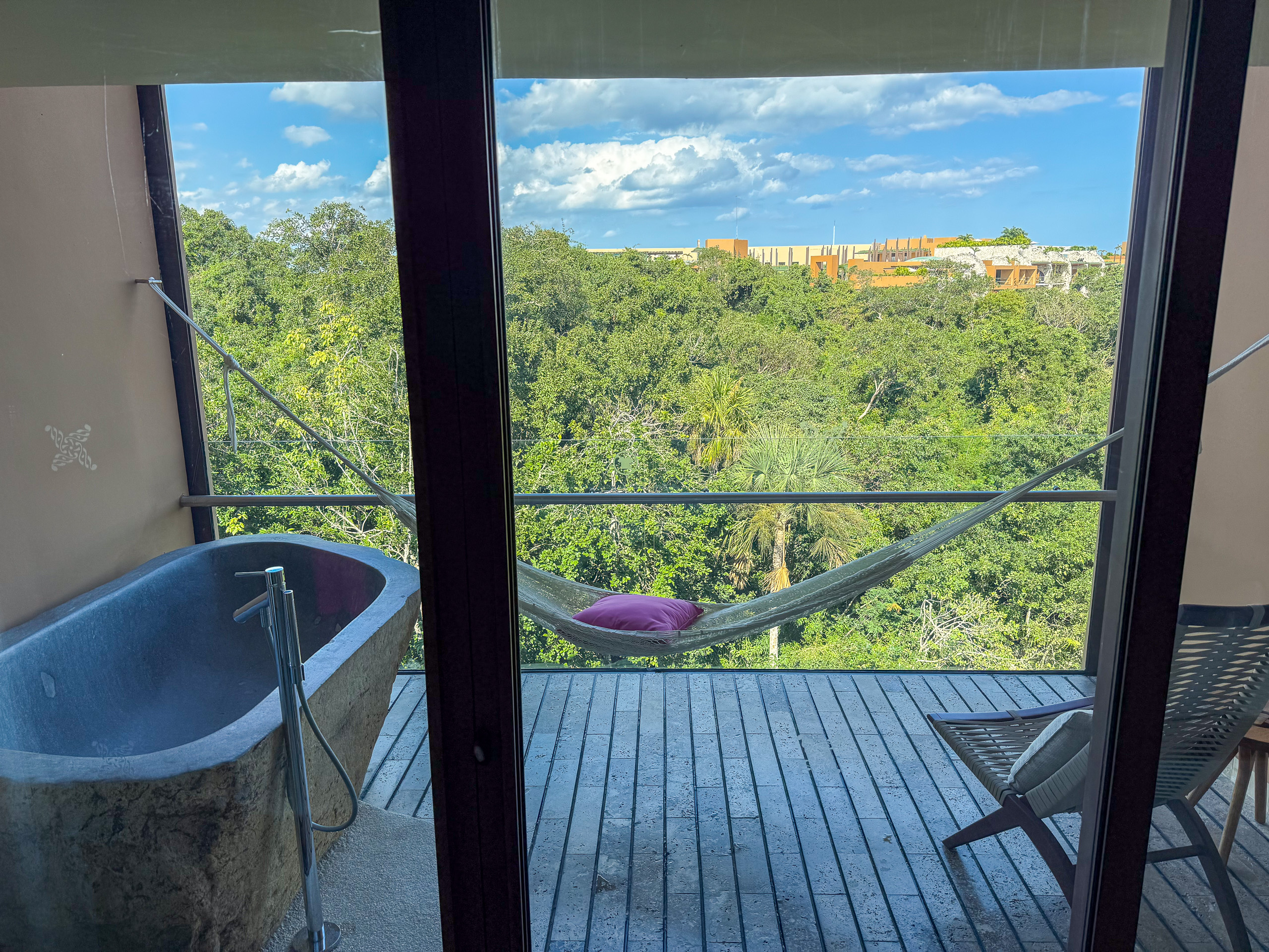 A freestanding bath at the window, a hammock strung on the deck and jungle beyond