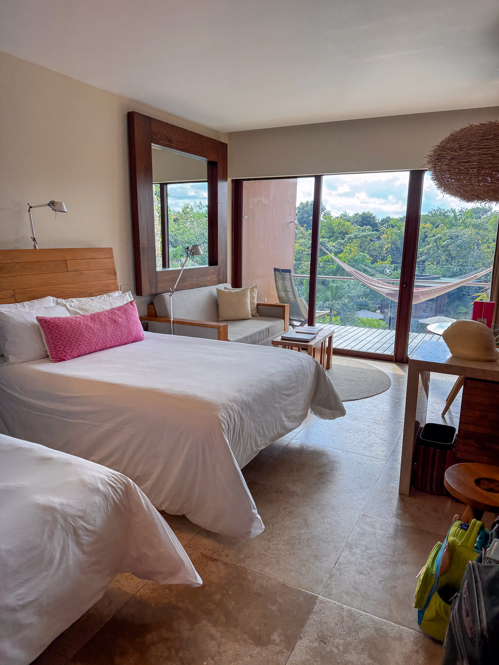 A bed made up in white against a wall of glass, the jungle pressing up outside