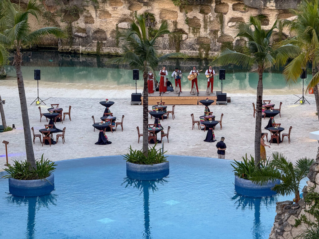 Performers in red on a stage across the water, palms lit behind them