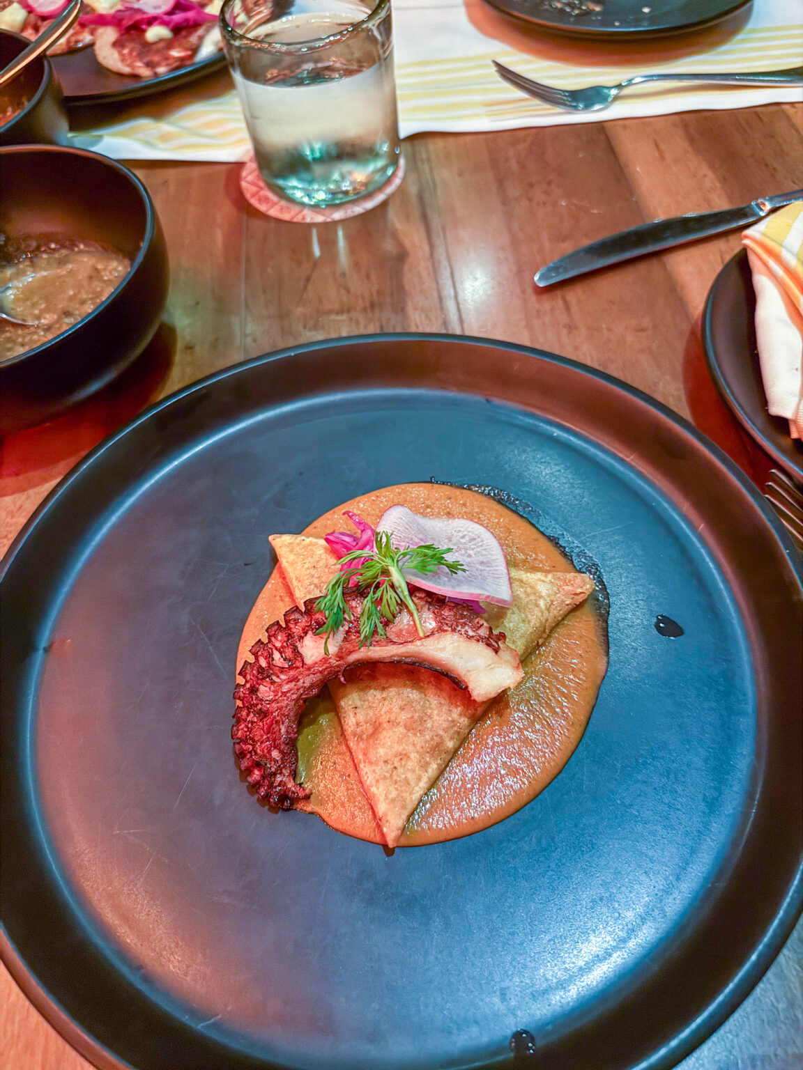 A folded tortilla filled with fish on a blue plate, the table set with dark bowls