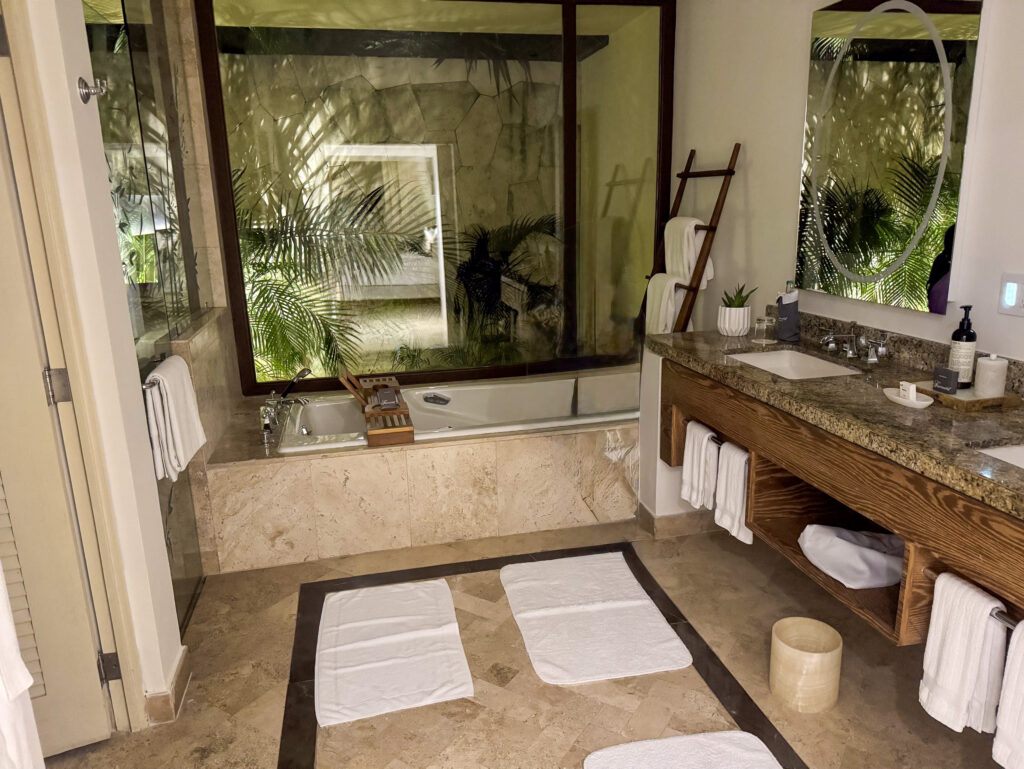 A bath under a window to the jungle, twin vanity and towels alongside
