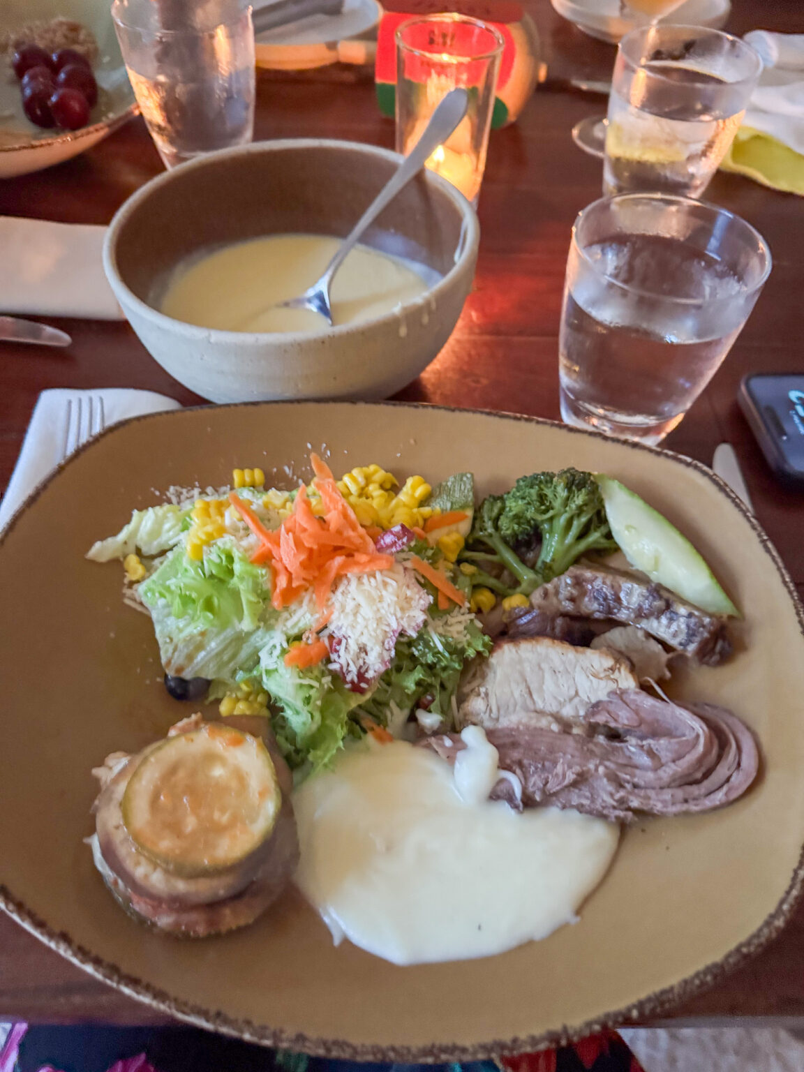 A plated lunch of sliced meat and vegetables with a bowl of soup alongside