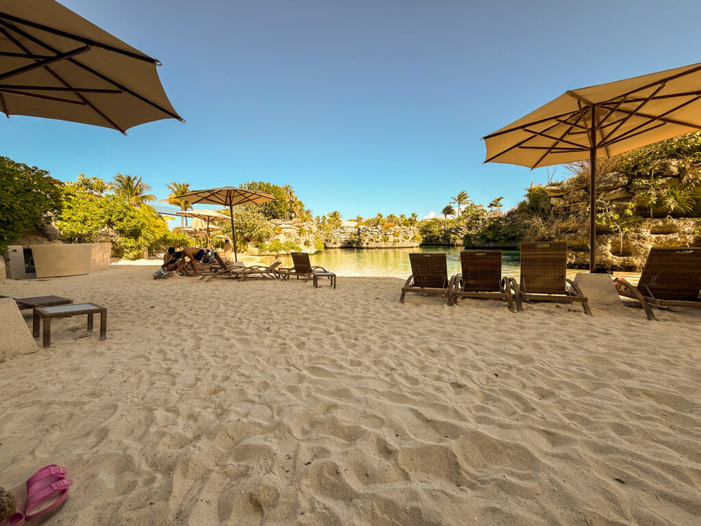 Cream umbrellas and loungers on the sand of a sheltered cove ringed by limestone rock and jungle